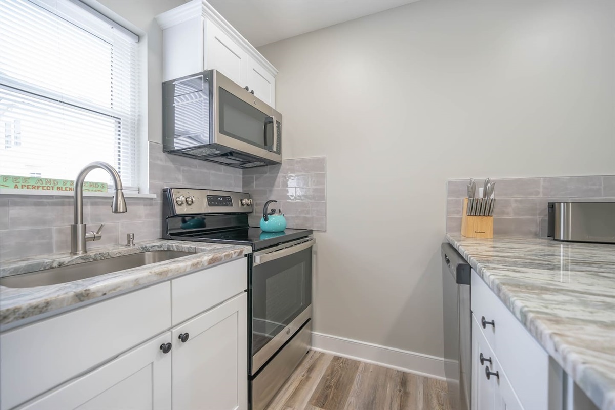 Well organized kitchen workspace with stainless steel appliances, stone counters, and ample prep space. Bright lighting and a clean layout make cooking simple and comfortable, whether preparing quick snacks or full meals during your stay.