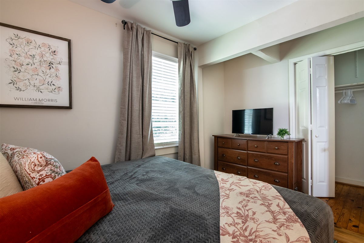 Charming bedroom setup with a warm and inviting design, complete with TV and dresser.