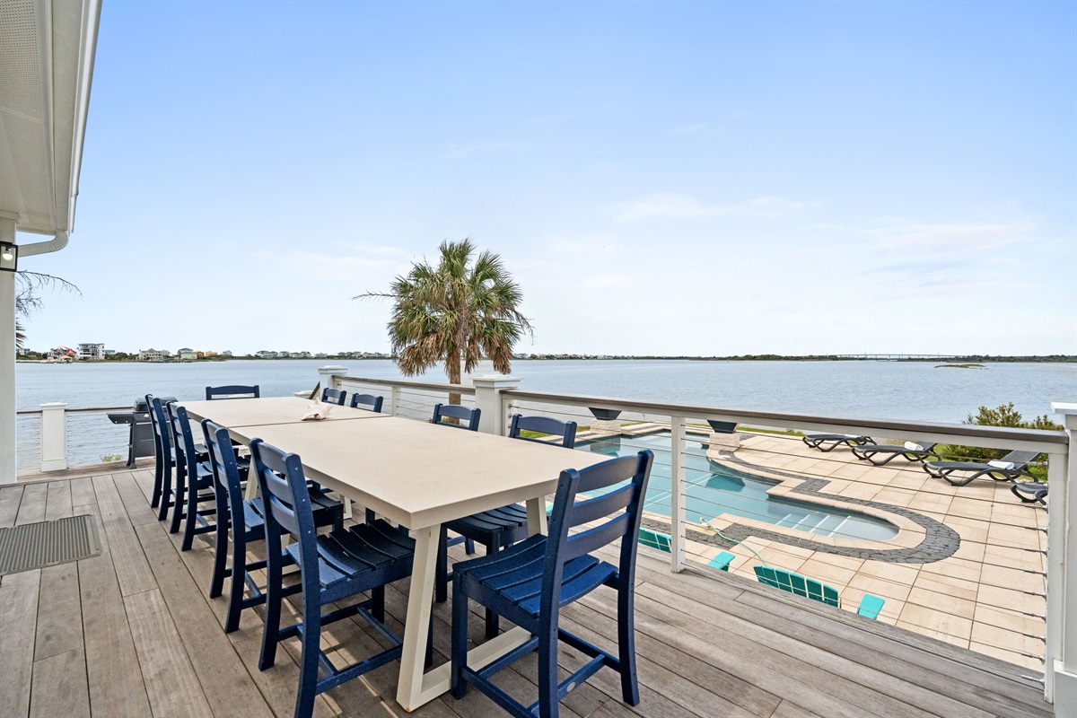 Outdoor dining deck with seating for the whole group overlooking the pool and water
