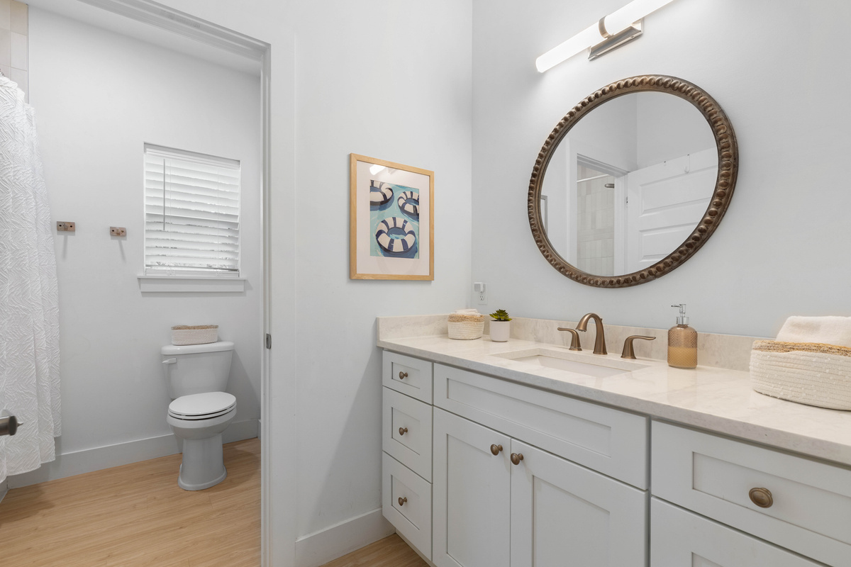 A long vanity with room for everybody's toothbrushes, a round mirror catching the light, and the toilet tucked into its own room behind the door - a small thing that keeps the mornings moving along nicely.