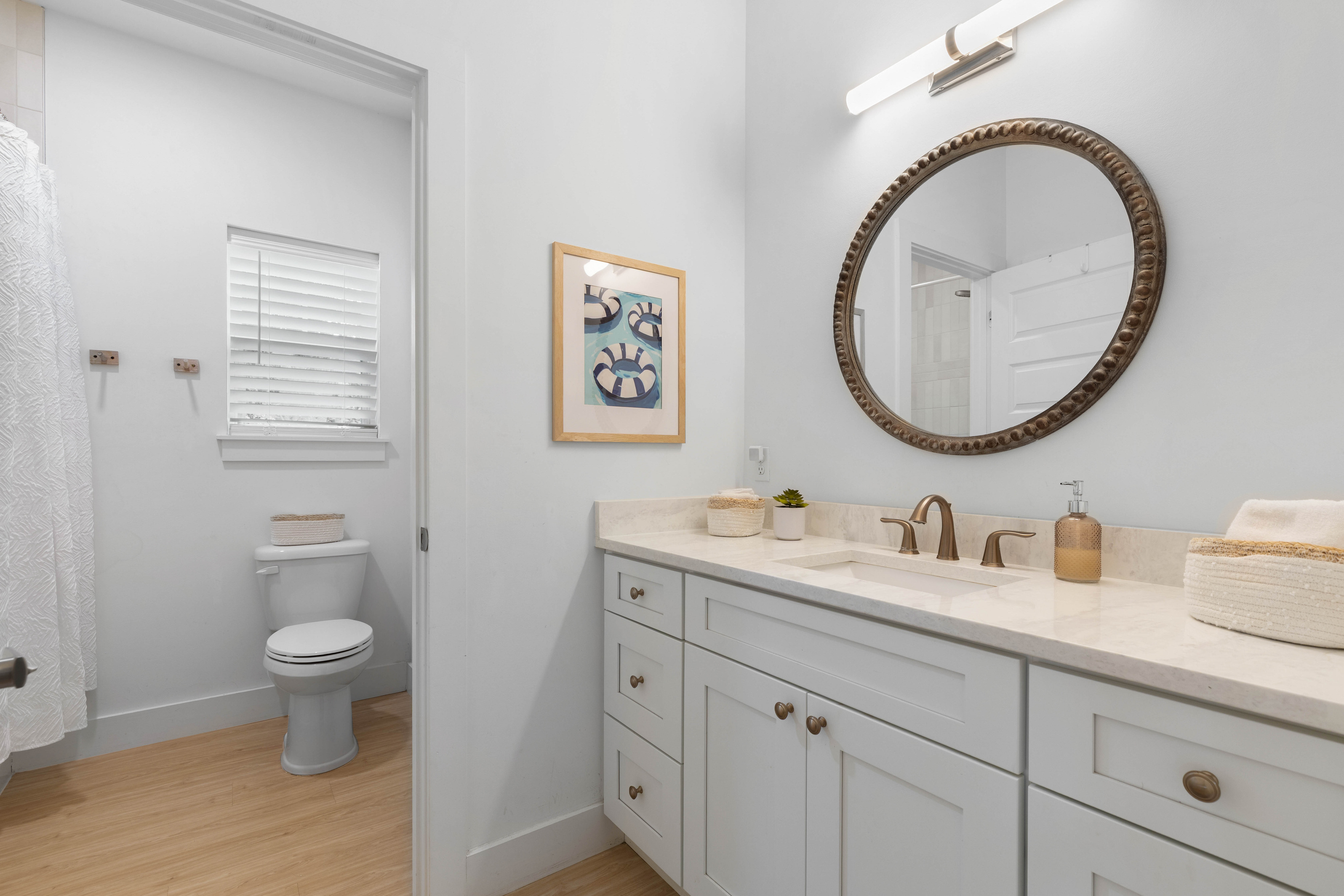 A long vanity with room for everybody's toothbrushes, a round mirror catching the light, and the toilet tucked into its own room behind the door - a small thing that keeps the mornings moving along nicely.