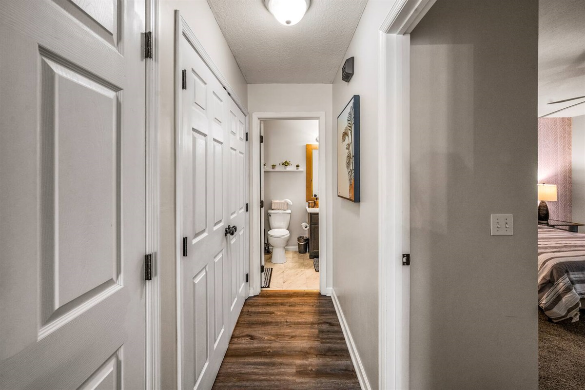 Bright hallway with wood flooring leading to a cozy bathroom and bedroom, offering a clean and welcoming transition space.