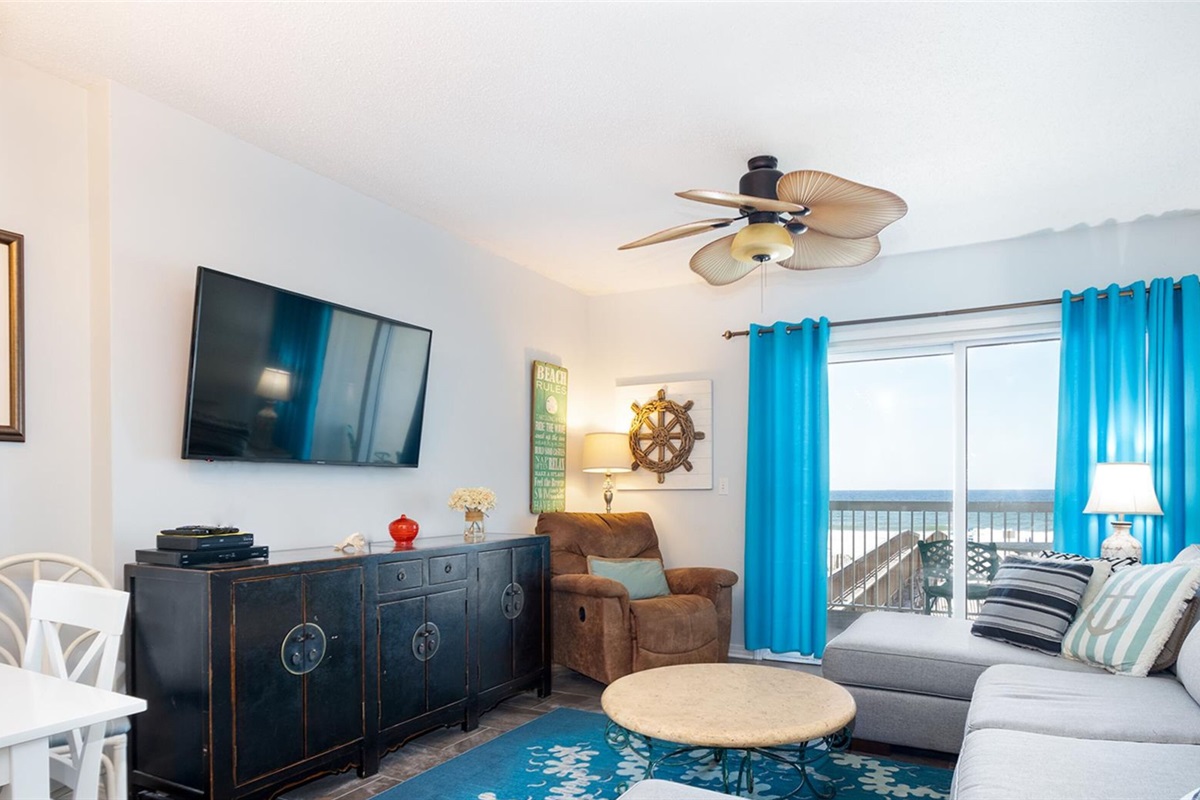Living room with wall mounted smart TV, ceiling fan, sleeper sofa and balcony access with breathtaking view