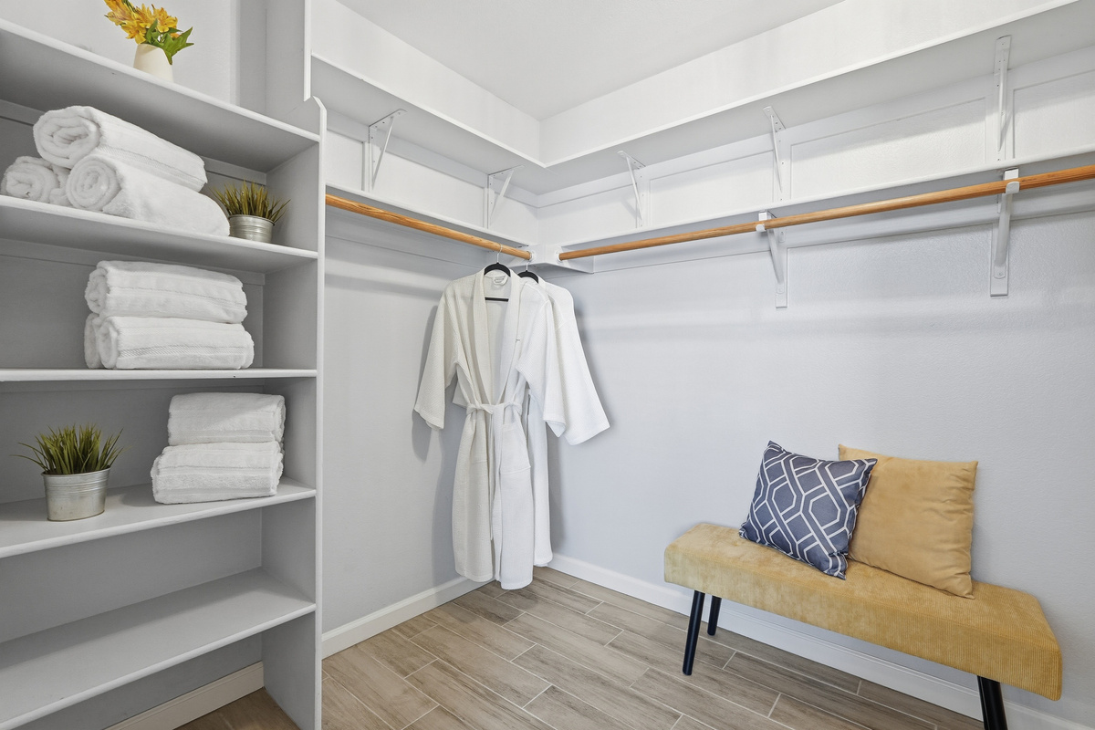 Walk-in closet with open shelving, hanging space, fresh towels, and a bench for easy unpacking during your stay.
