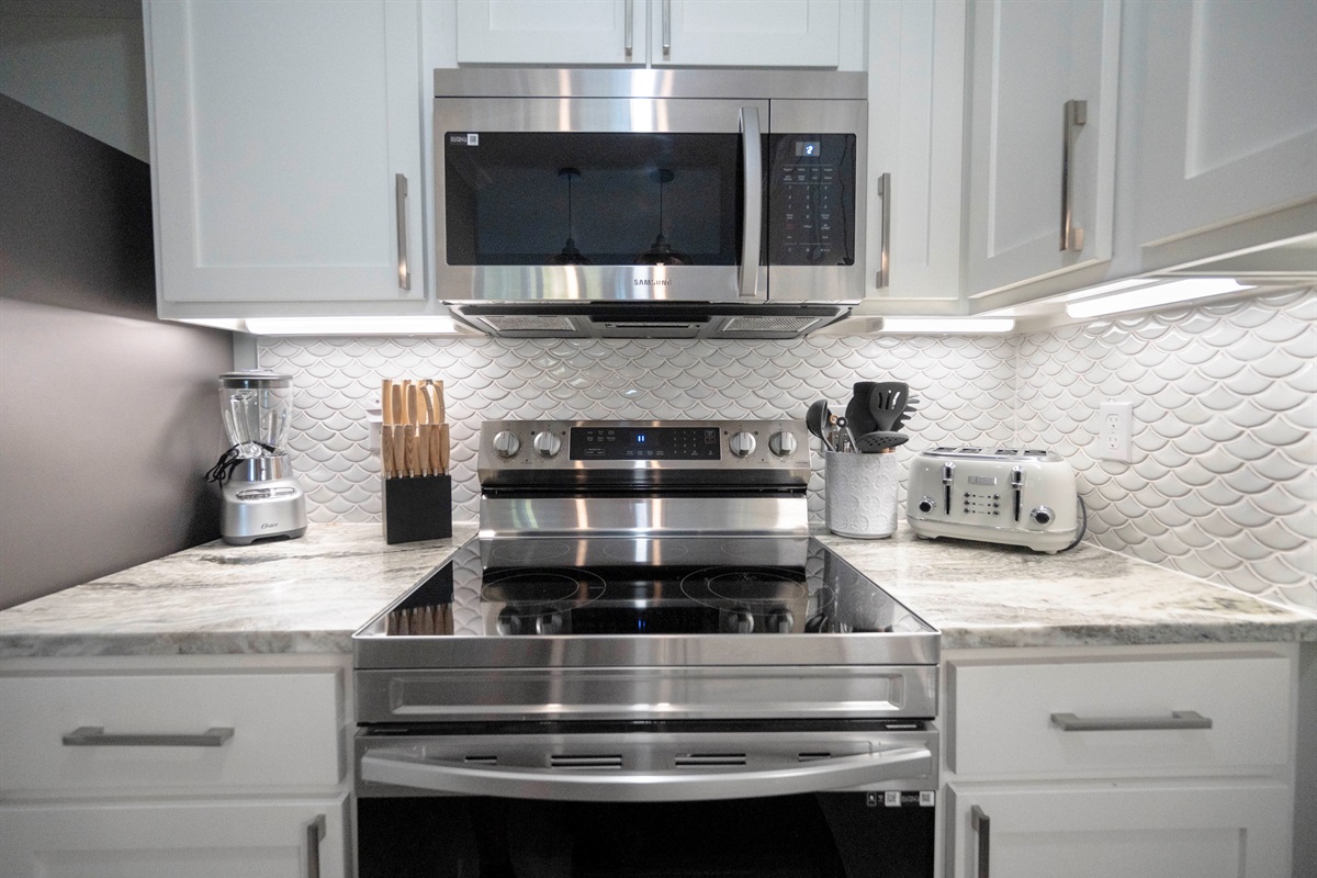 A modern kitchen with white cabinets, stainless appliances, and a sleek fish-scale backsplash for elegance.
