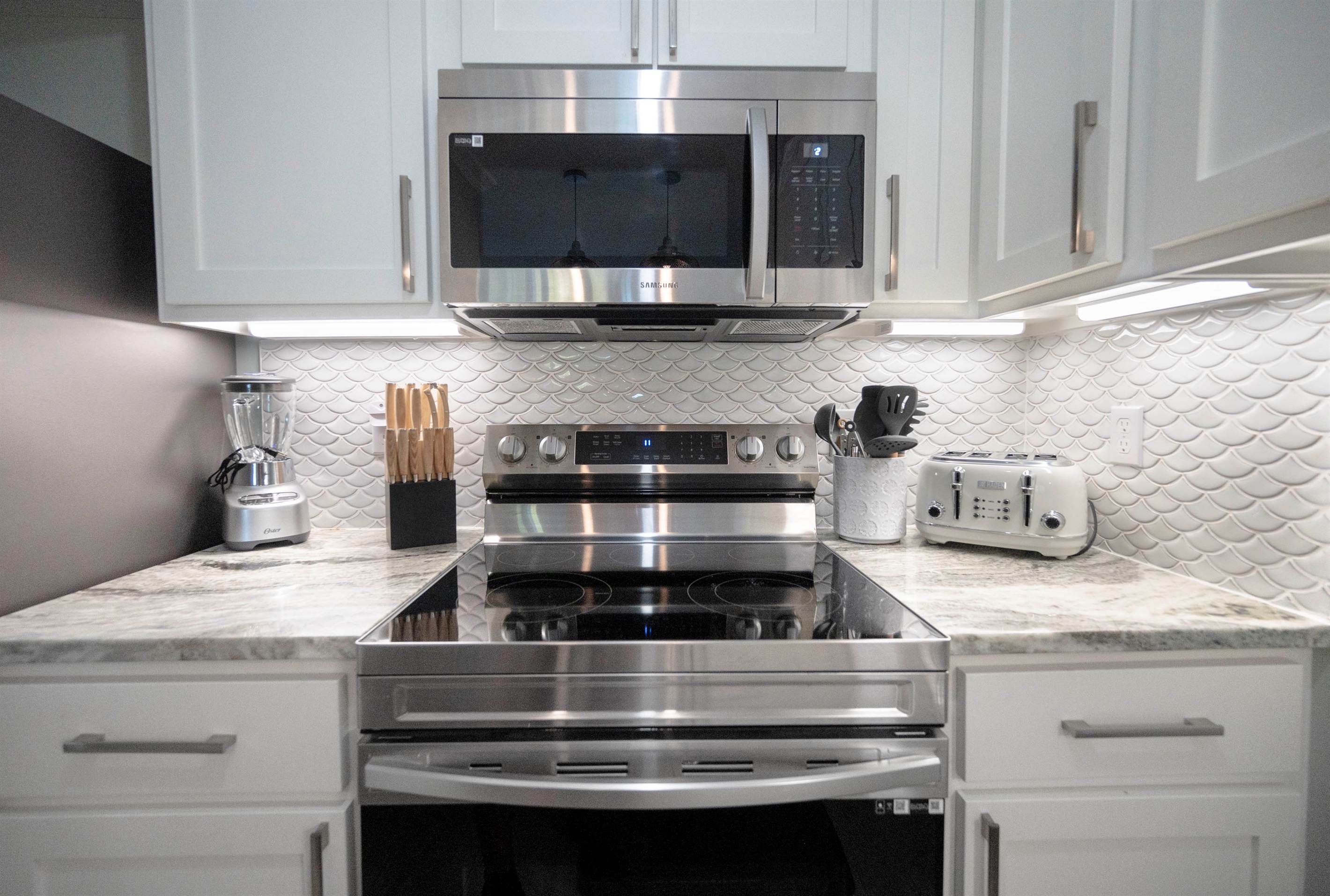A modern kitchen with white cabinets, stainless appliances, and a sleek fish-scale backsplash for elegance.
