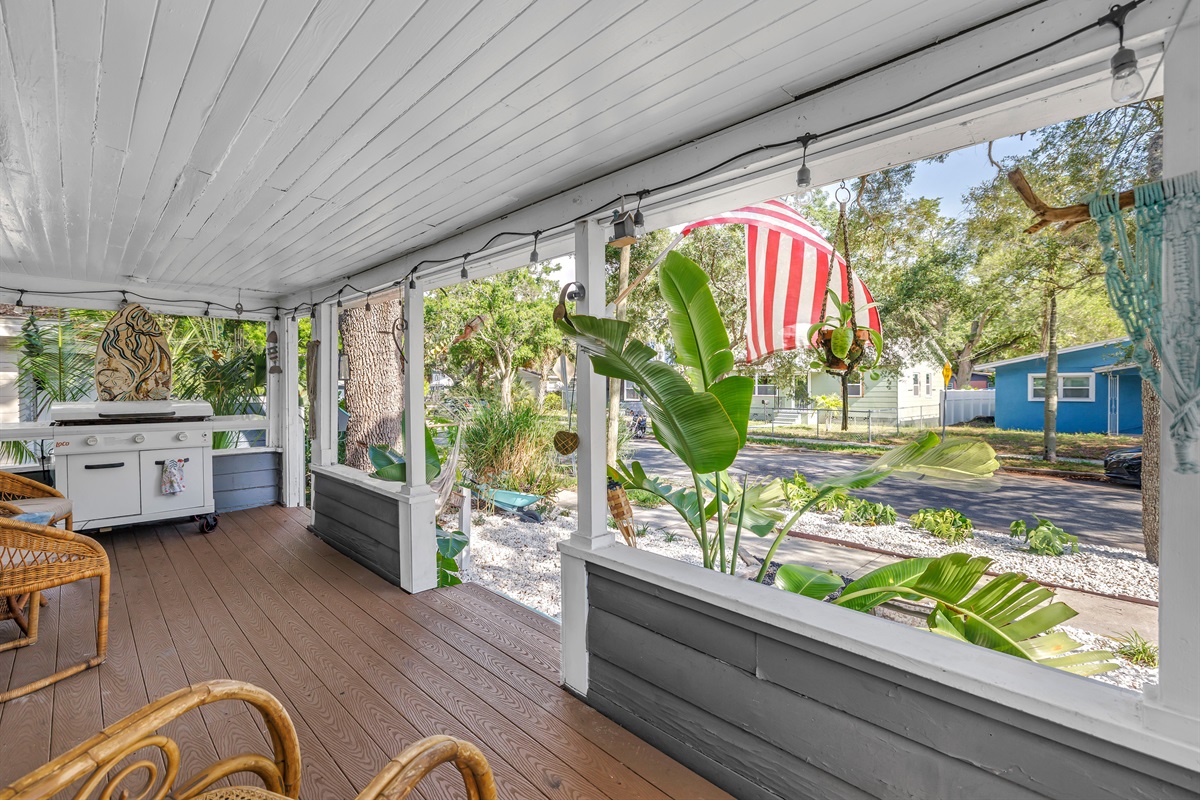 porch with cozy seating, string lights, and a peaceful view of the fenced yard and tropical landscaping.