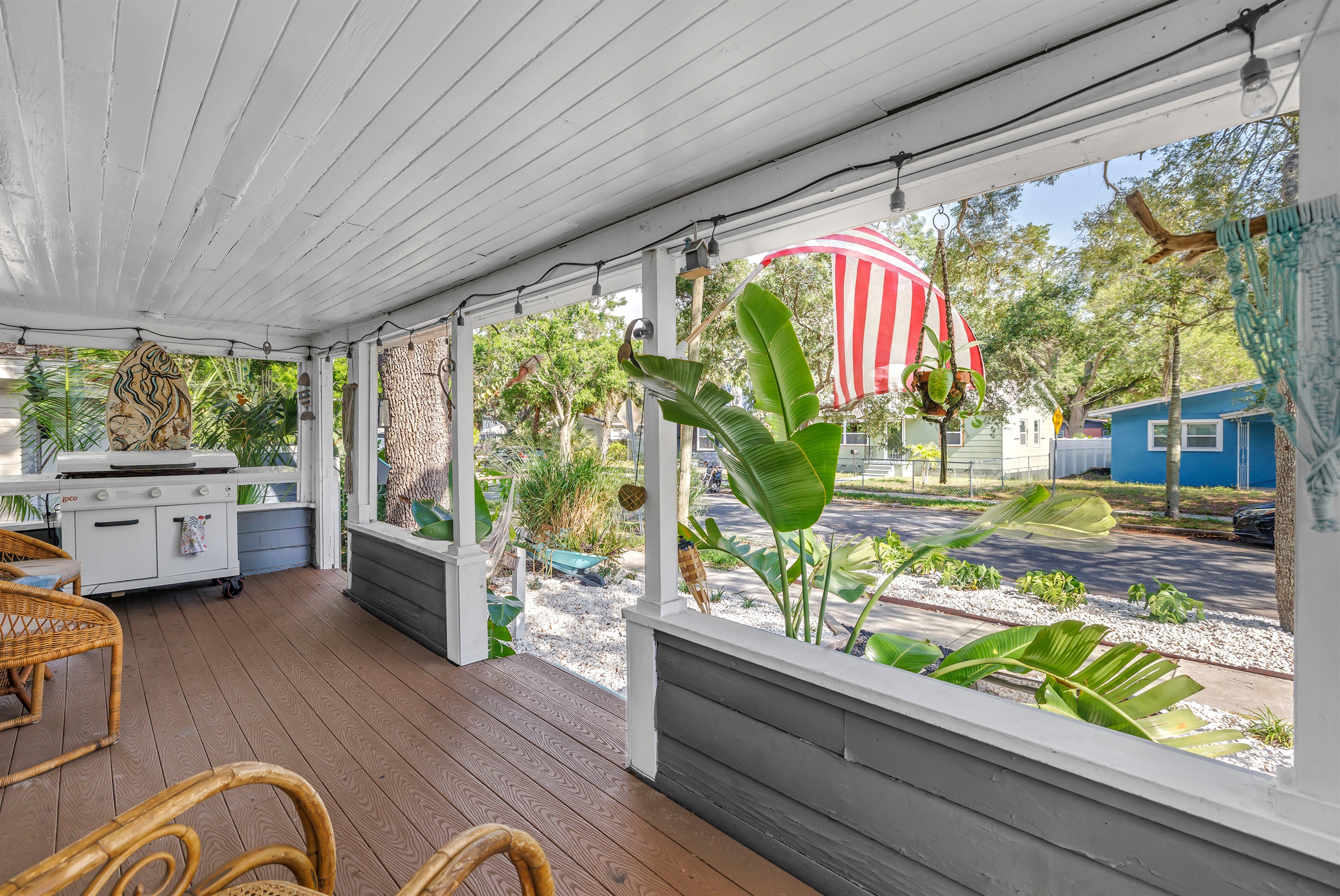 porch with cozy seating, string lights, and a peaceful view of the fenced yard and tropical landscaping.