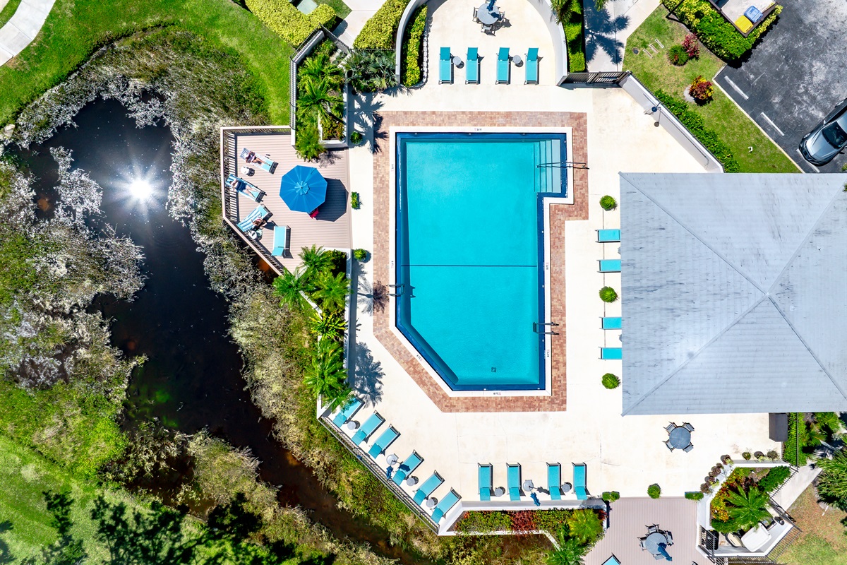 Resort-style heated community pool surrounded by lush tropical landscaping, sun loungers, and peaceful lake views — perfect for relaxing after a day at the beach or golf course.
