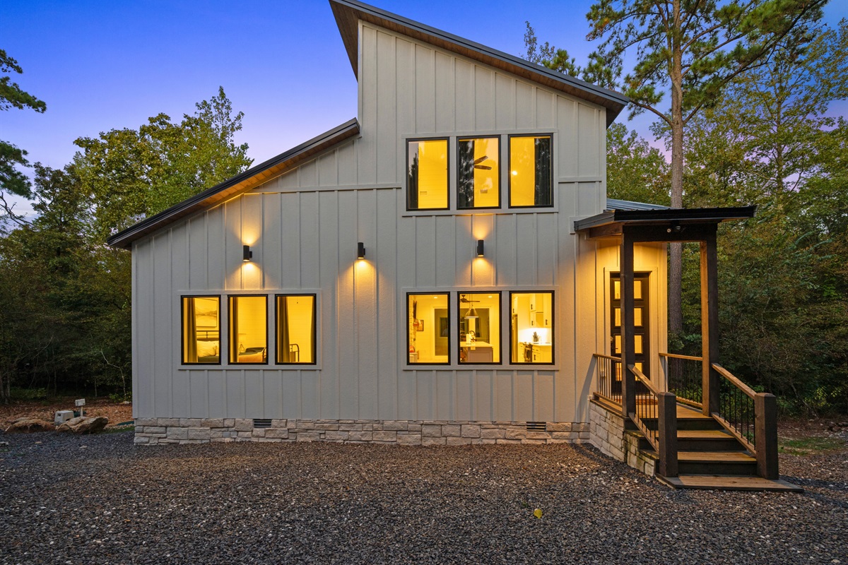 A welcoming view of the cabin from the driveway shows the clean modern design and warm lighting in the evening.