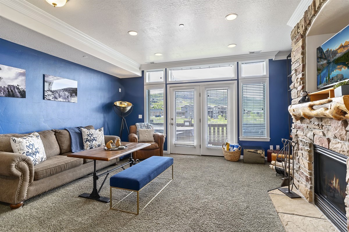 A vibrant, designer-inspired living room where rich tones, plush seating, and a striking stone fireplace create an inviting space to unwind in elevated comfort with incredible mountain views. 