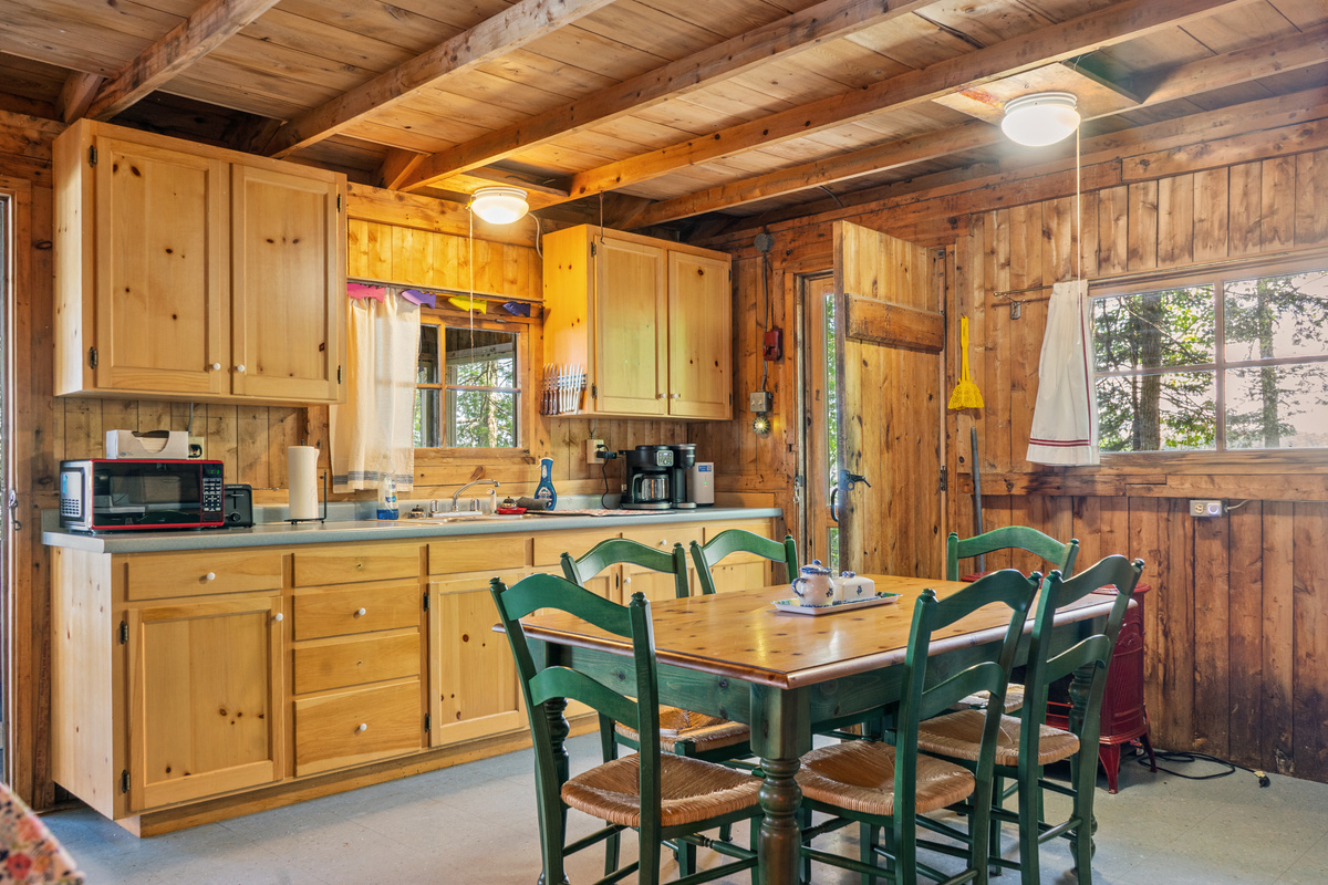 Kitchen and dining area at Loonrise Point! Green-trimmed dining table seats guests right alongside the fully stocked kitchen counters, pass-through window, microwave, and coffee maker. Rustic Maine camp style on Beech Hill Pond in Otis, ME.