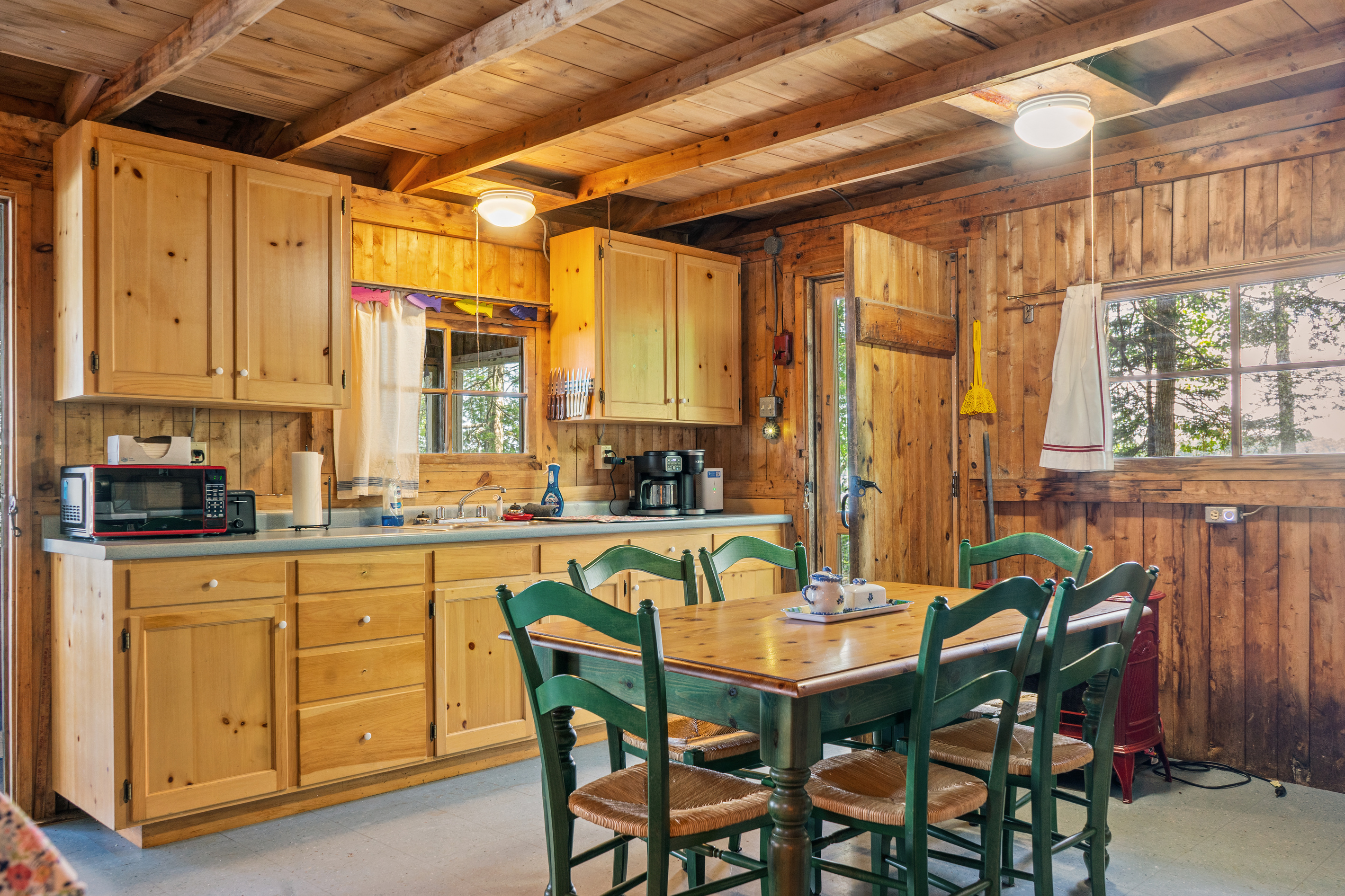 Kitchen and dining area at Loonrise Point! Green-trimmed dining table seats guests right alongside the fully stocked kitchen counters, pass-through window, microwave, and coffee maker. Rustic Maine camp style on Beech Hill Pond in Otis, ME.