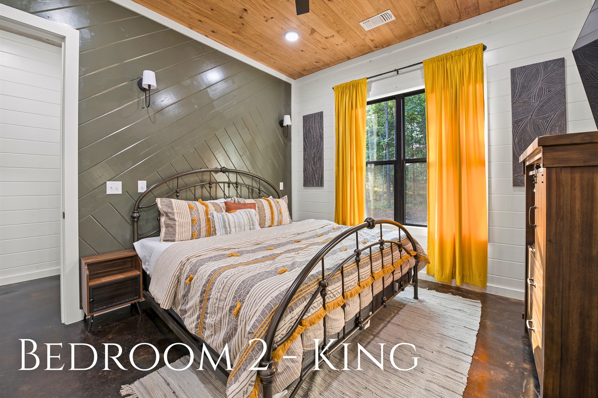 A spacious bedroom featuring a king-sized bed, accentuated with unique yellow drapes that complement the dark green wall