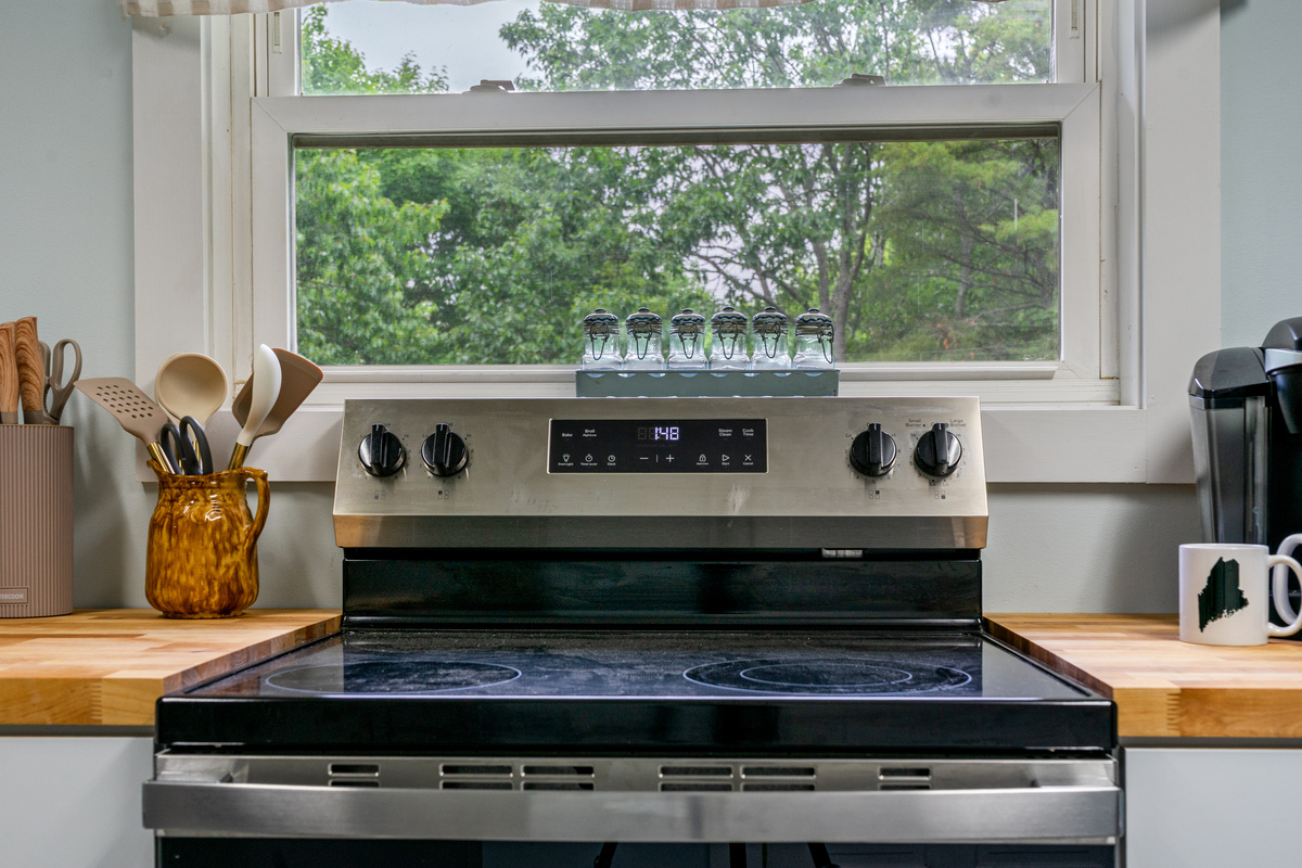 Enjoy a bright, scenic view while preparing meals for your group. This close-up shows the clean GE electric range with its smooth glass cooktop, flanked by warm butcher block surfaces and essential cooking utensils for a seamless culinary experience.