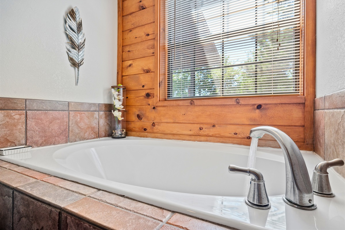 Relax and recharge in this deep soaking tub with forest views through the window.