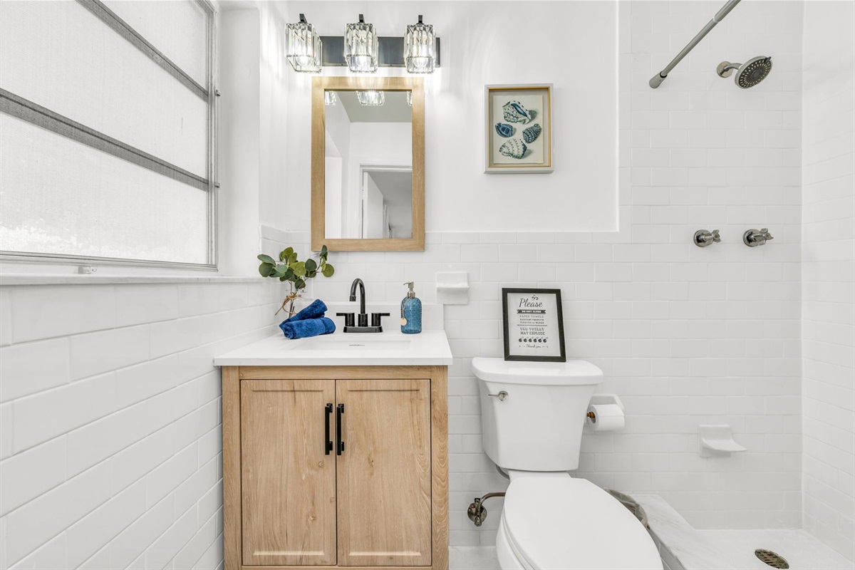A serene, spa-like ensuite showcasing a chic wood vanity, elegant lighting, modern black hardware, and a pristine walk-in shower for total comfort.