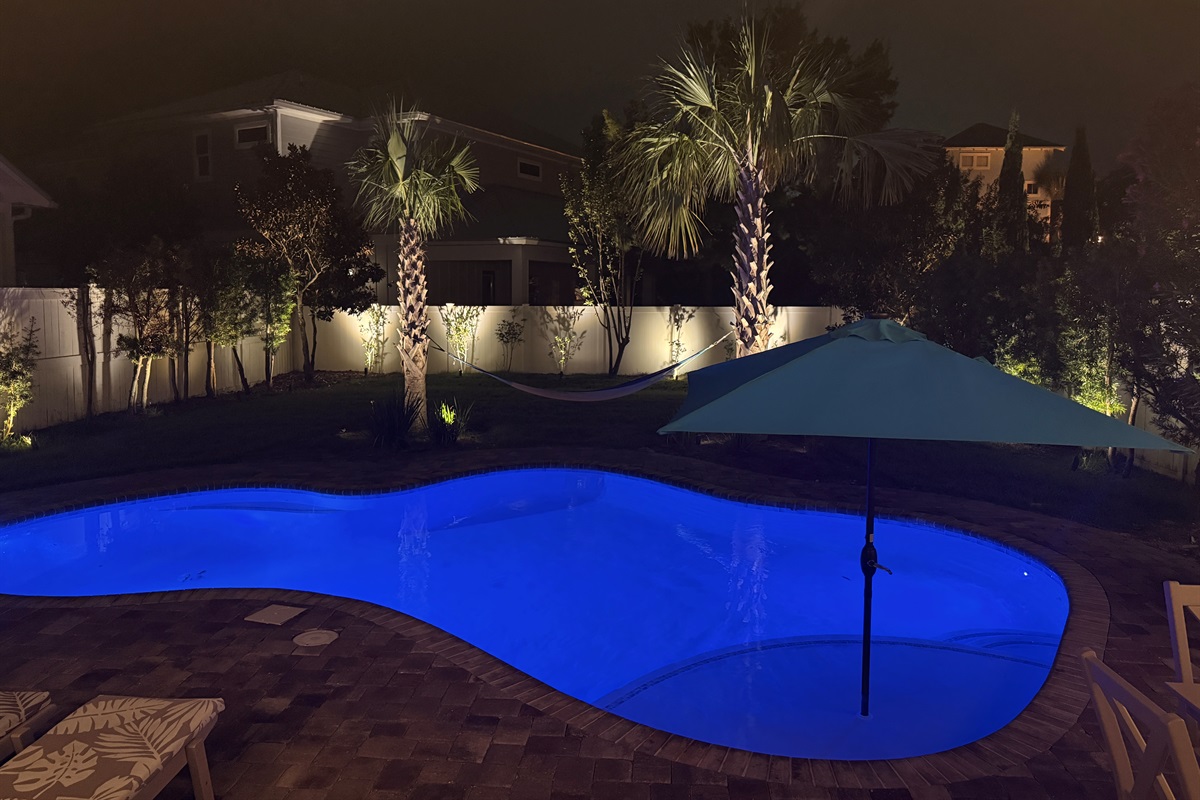 Evening pool view showcasing ambient lighting and a peaceful backyard setting.