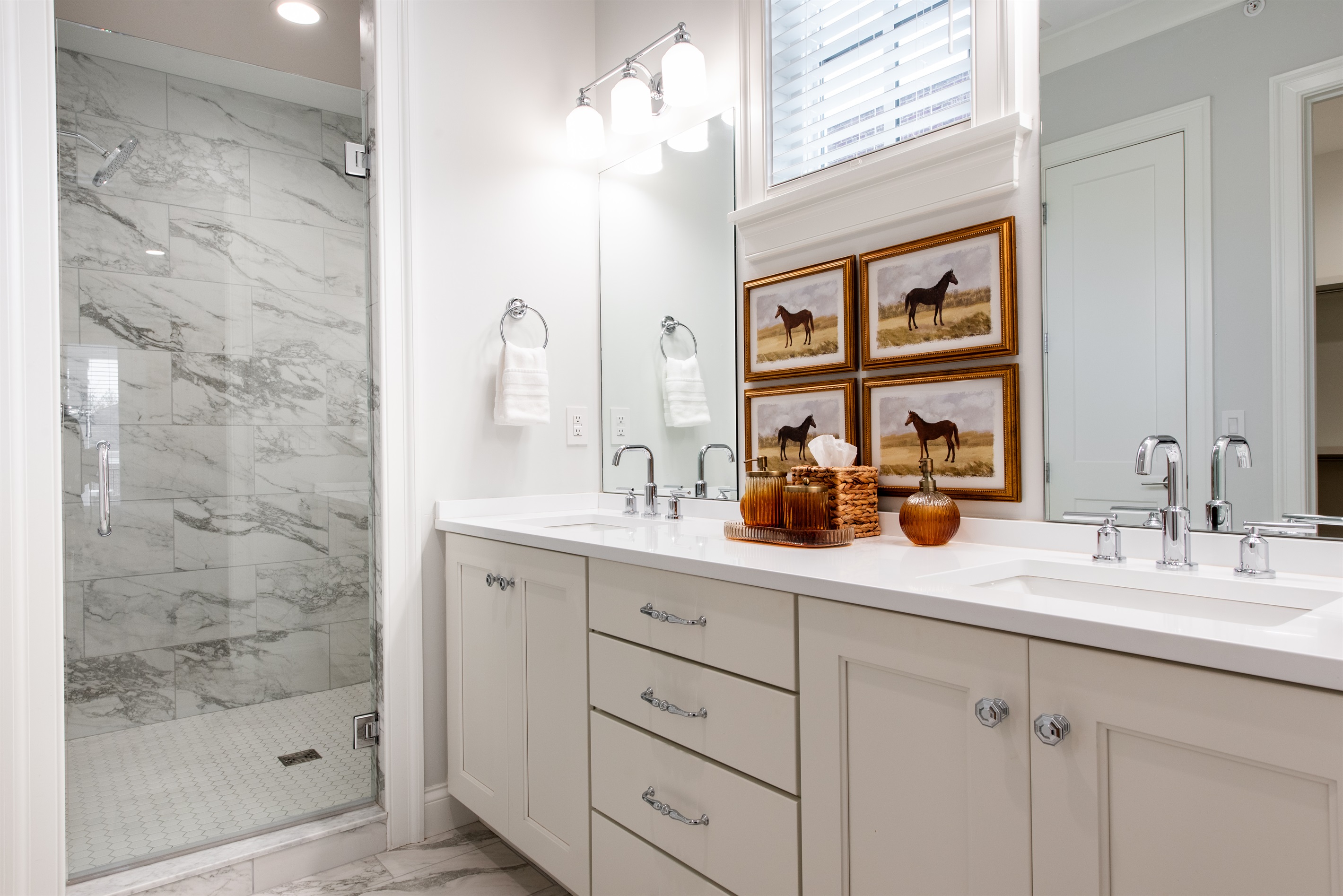 Step into a beautifully designed bathroom featuring dual vanities, marble tile, and a walk-in shower. Enjoy the sophisticated decor with horse-themed artwork, adding a touch of Kentucky's charm to your stay. Perfect for a relaxing retreat.