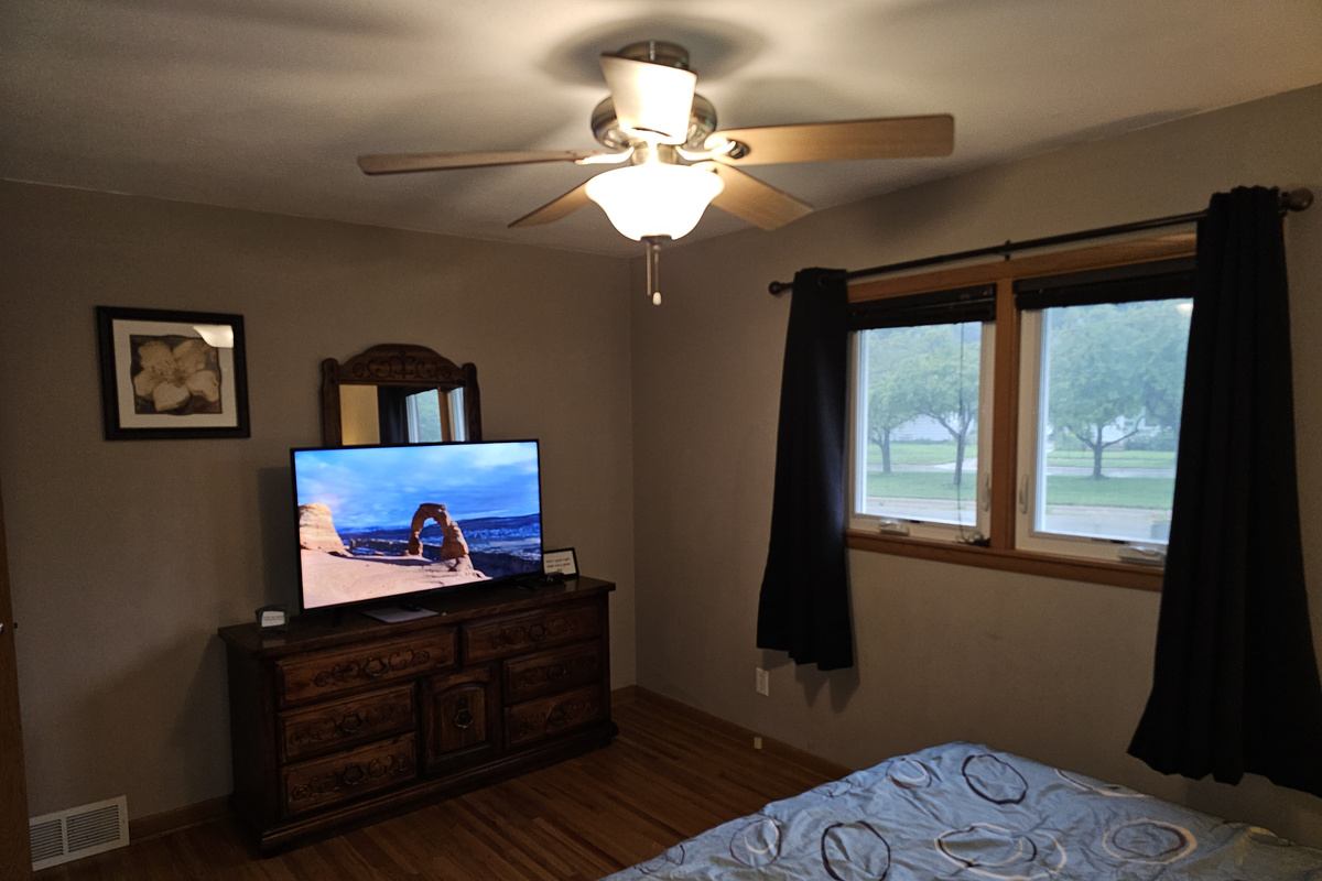 Master bedroom on the main floor with king bed, ceiling fan, alarm clock and a smart tv.