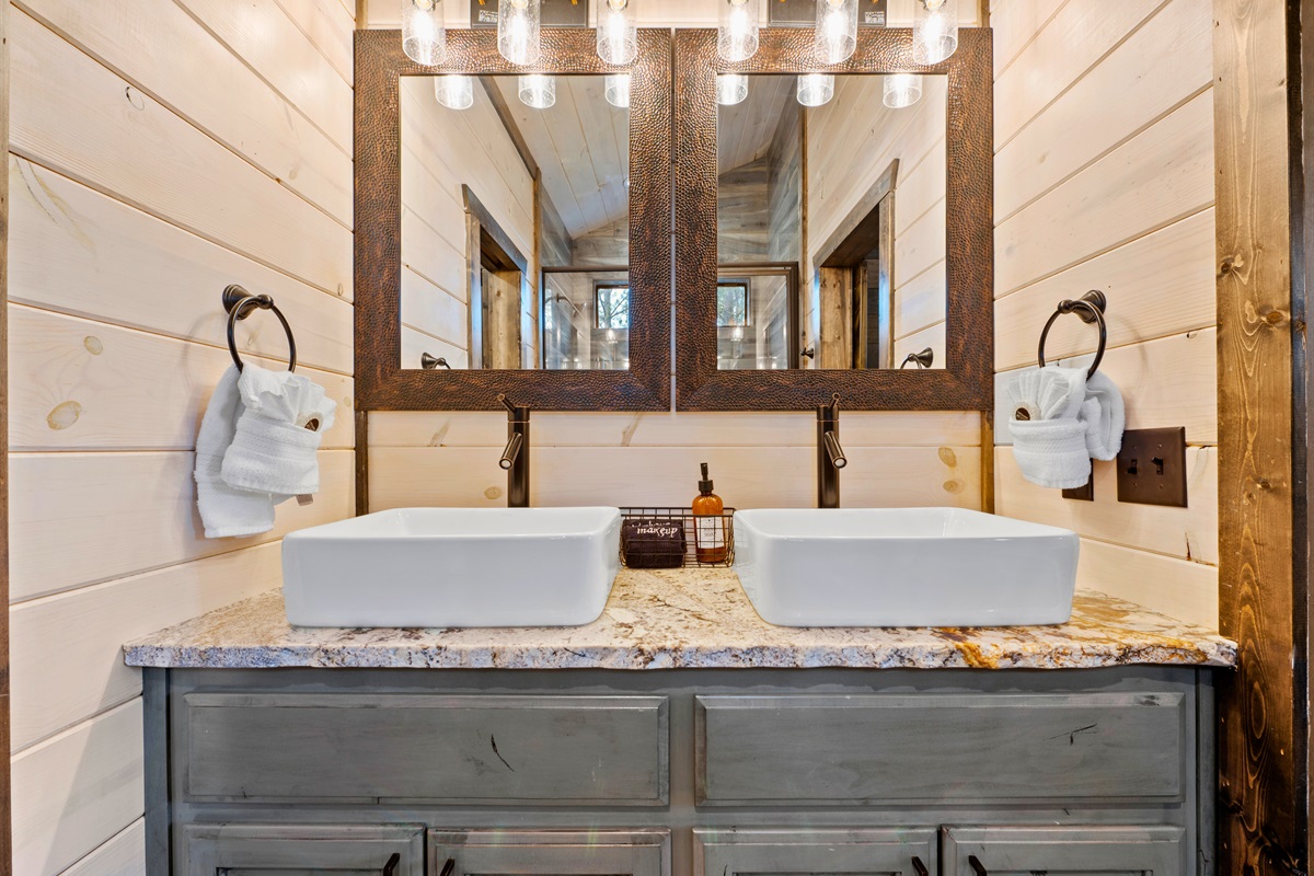 A closer look at the bathroom's vanity area highlights twin vessel sinks with a wooden-style mirror