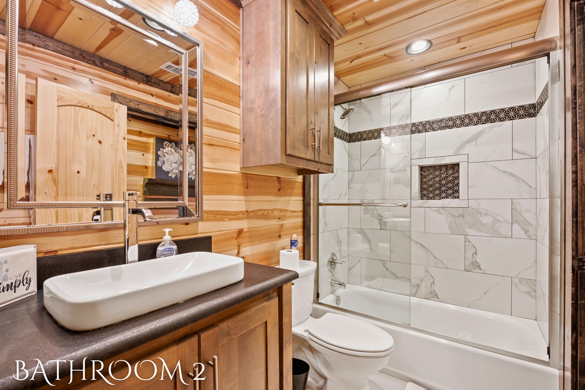 This bathroom showcases a combination of marble tiling and warm wood accents, featuring a stylish vessel sink and a tub-shower setup.