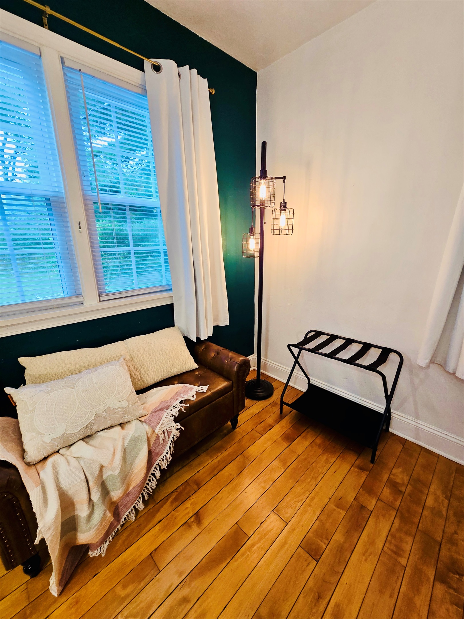 Cozy layers and garden views—our cushioned bench in Queen’s Landing invites you to curl up and unwind. Soft blankets, plush pillows, a handy luggage rack, and those gorgeous hardwood floors complete the scene.