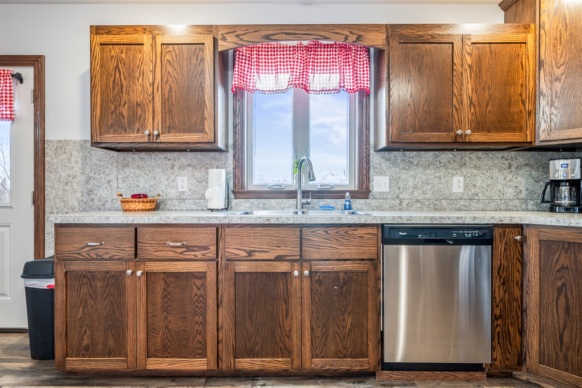 Bright kitchen with double sink, dishwasher, and large window overlooking the yard.