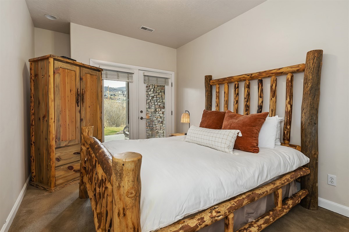 A beautifully styled lower-level bedroom with a queen bed, blending rustic charm with cozy comfort with easy outdoor access.