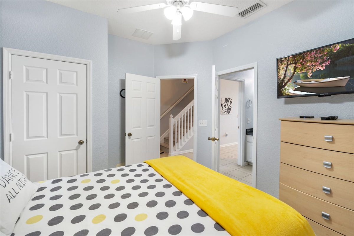 - Bright bedroom with modern polka dot bedding and cheerful yellow throw  
- Wall mounted TV and dresser provide convenience and entertainment  
- Access to hallway and stairway for easy movement throughout the home  
