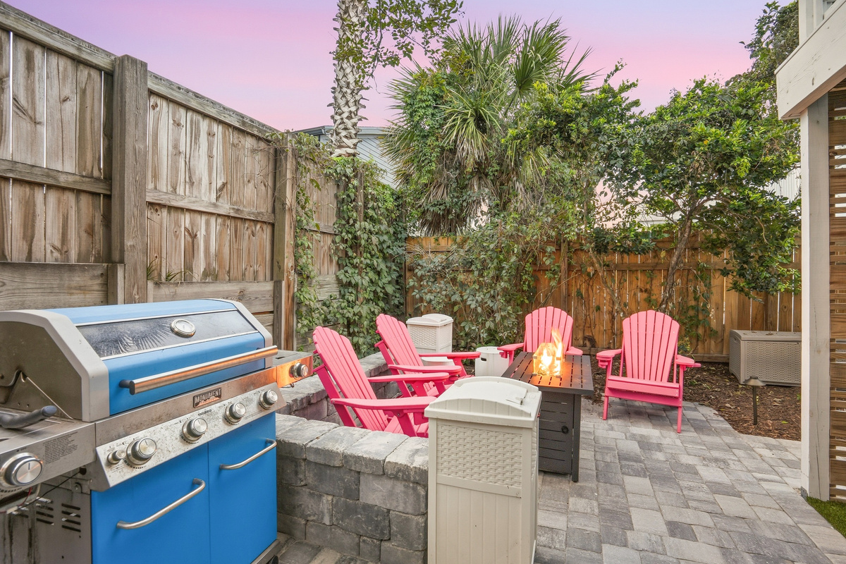 Here’s a view of the cozy, tropical backyard—lush and inviting with a grill, firepit, and patio area. You’ll even spot a lime tree, adding a fresh touch to this serene outdoor space!