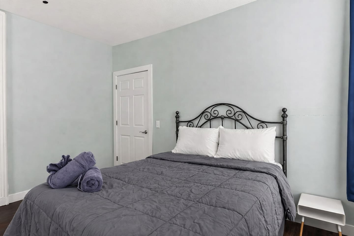 Cozy sleeping space with queen-size bed, side table, and tall windows that fill the room with daylight.