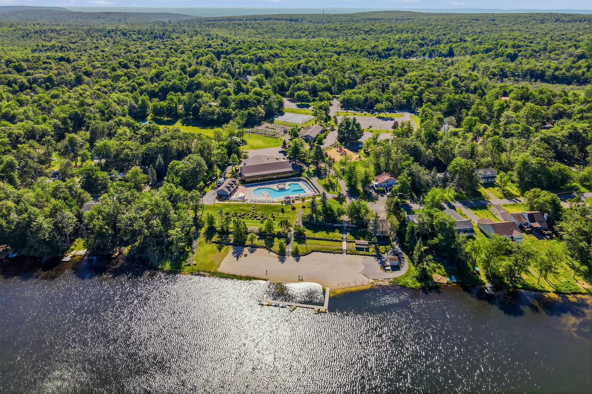 Aerial drone view of the Pocono Country Place community — lake, pool, and wooded lots