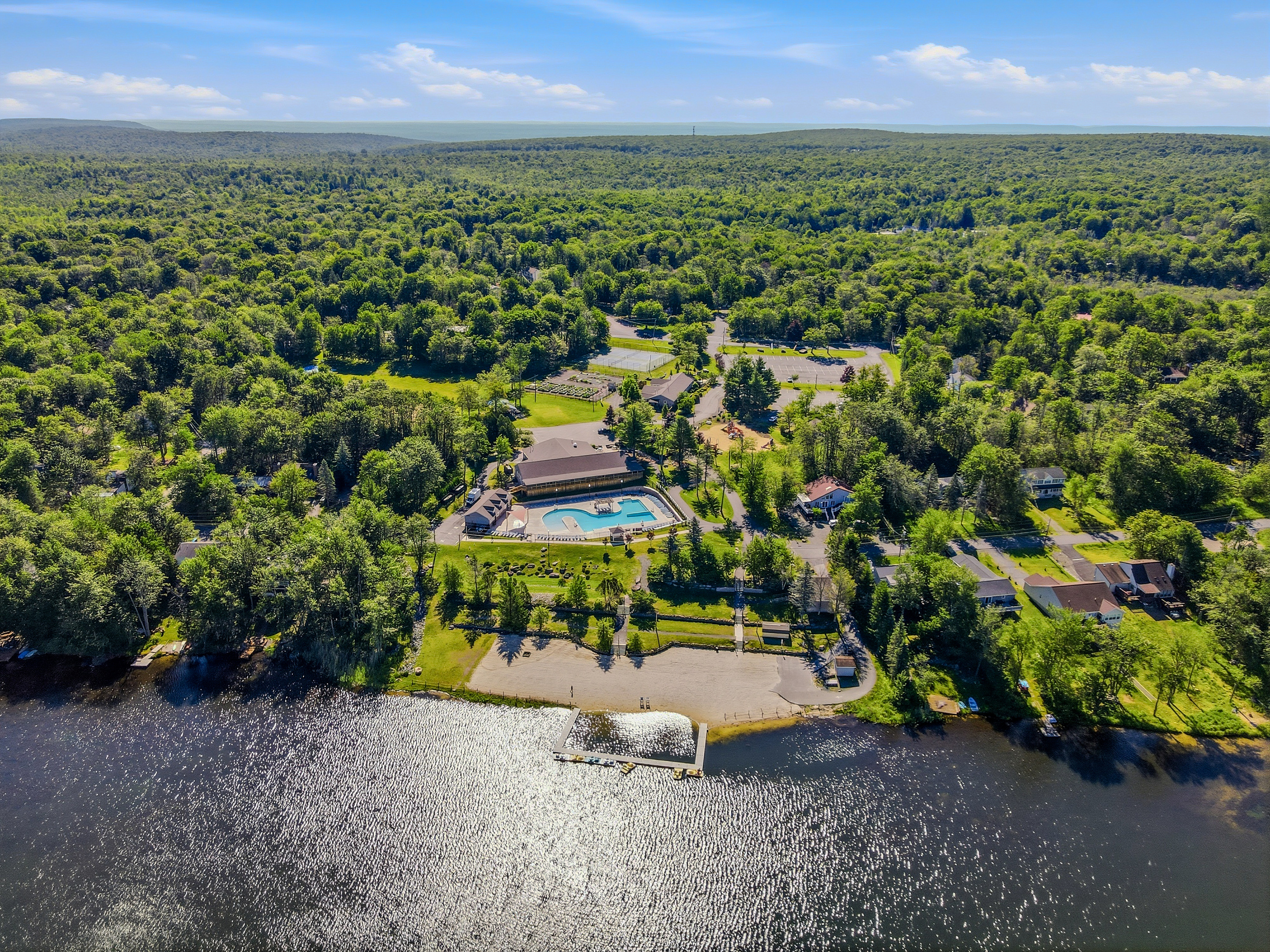Aerial drone view of the Pocono Country Place community — lake, pool, and wooded lots