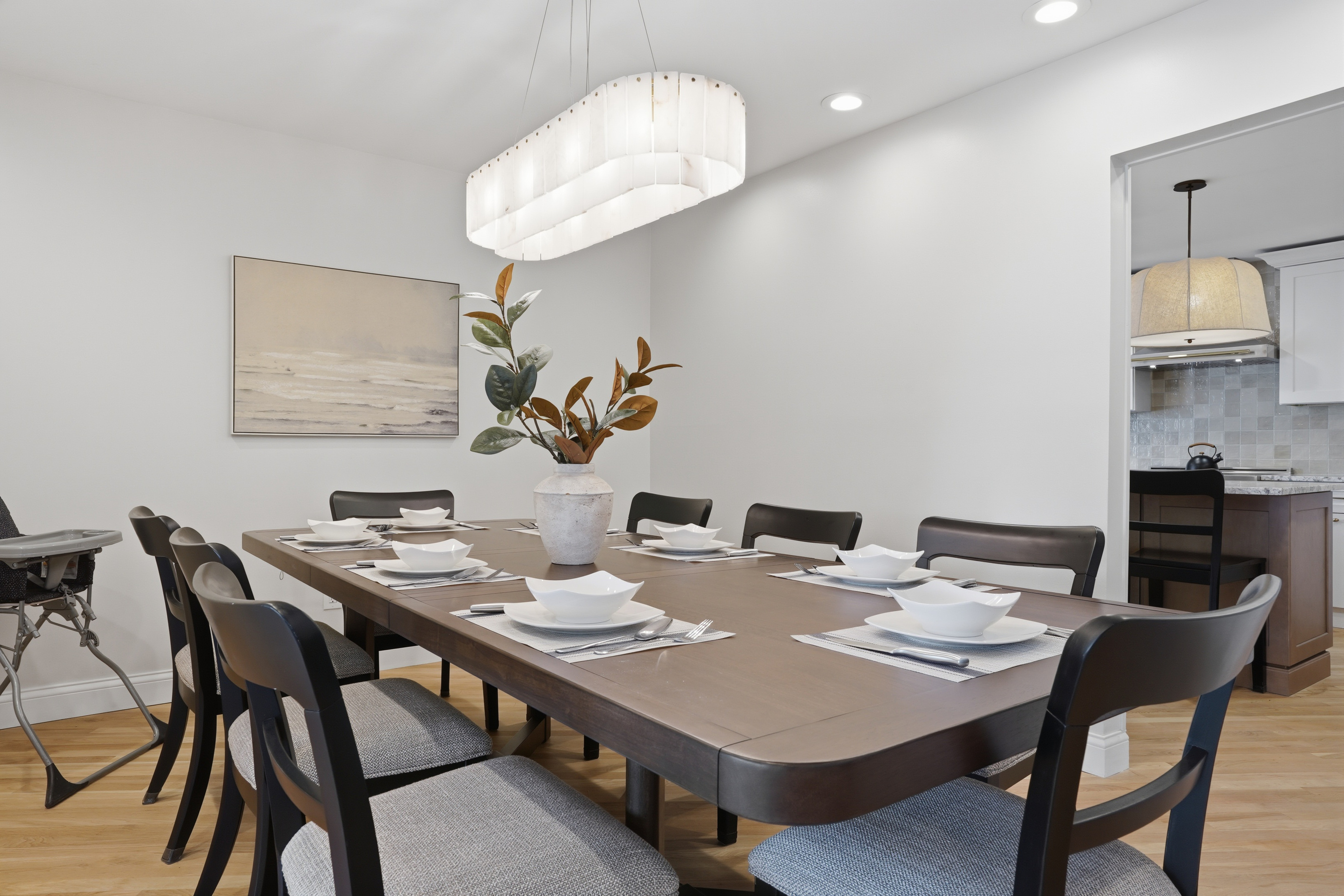 Elegant dining area with a large table, modern seating, and statement lighting. Clean, stylish space perfect for family meals or group gatherings in a bright, upscale setting.