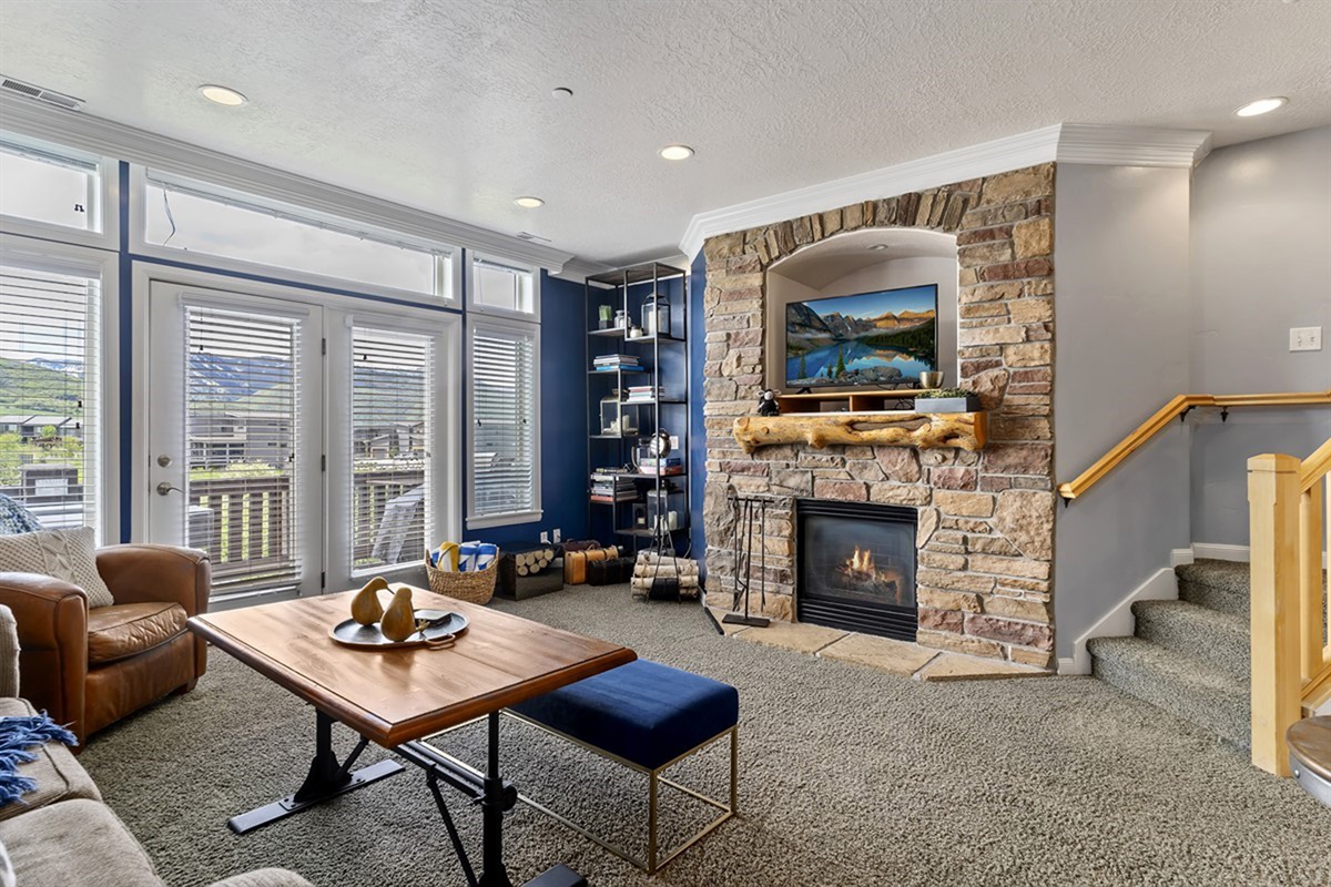 This expansive living area blends warmth and sophistication, featuring a statement stone fireplace, abundant natural light, and seamless access to outdoor living.
