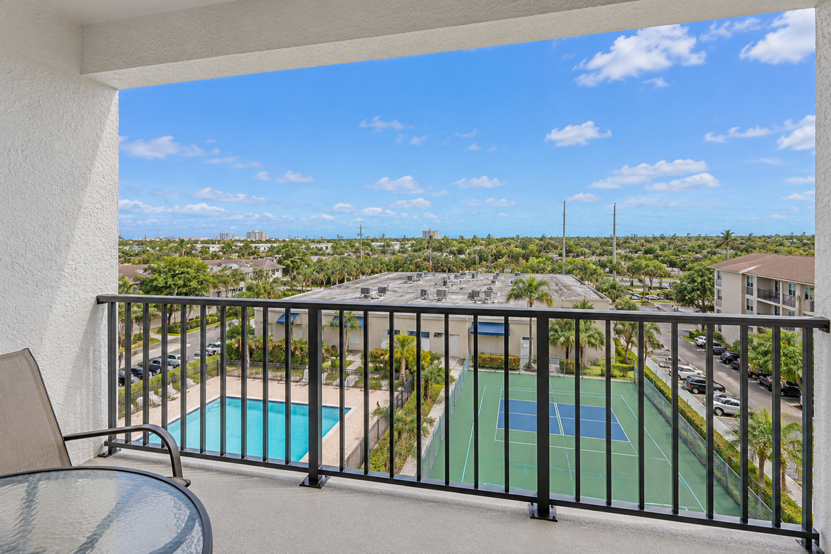 Covered balcony with table seating, chairs, and a treetop view over the Holiday Towers area.