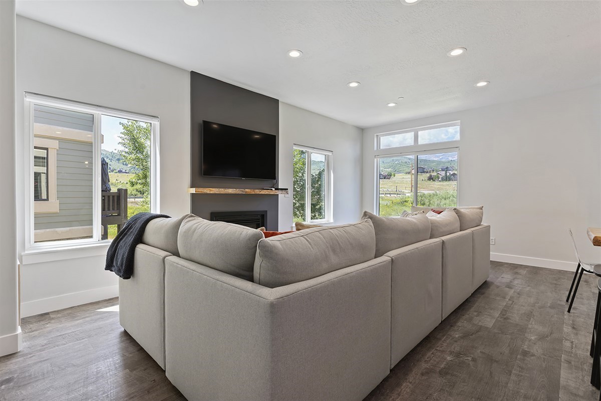 Relax in the inviting living room with plush seating, a warm fireplace, and large windows framing scenic outdoor mountain views.