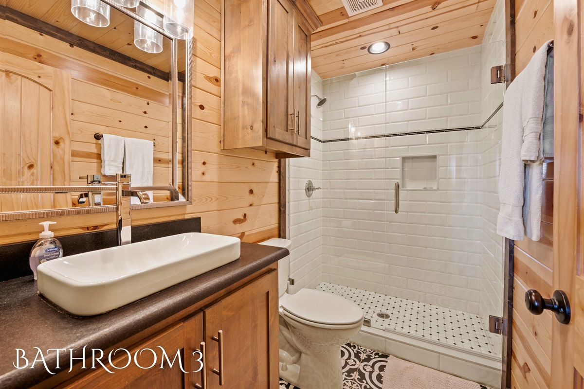 A neatly designed bathroom featuring a rectangular sink on a wooden vanity, complemented by a subway-tiled shower and rustic light fixtures.