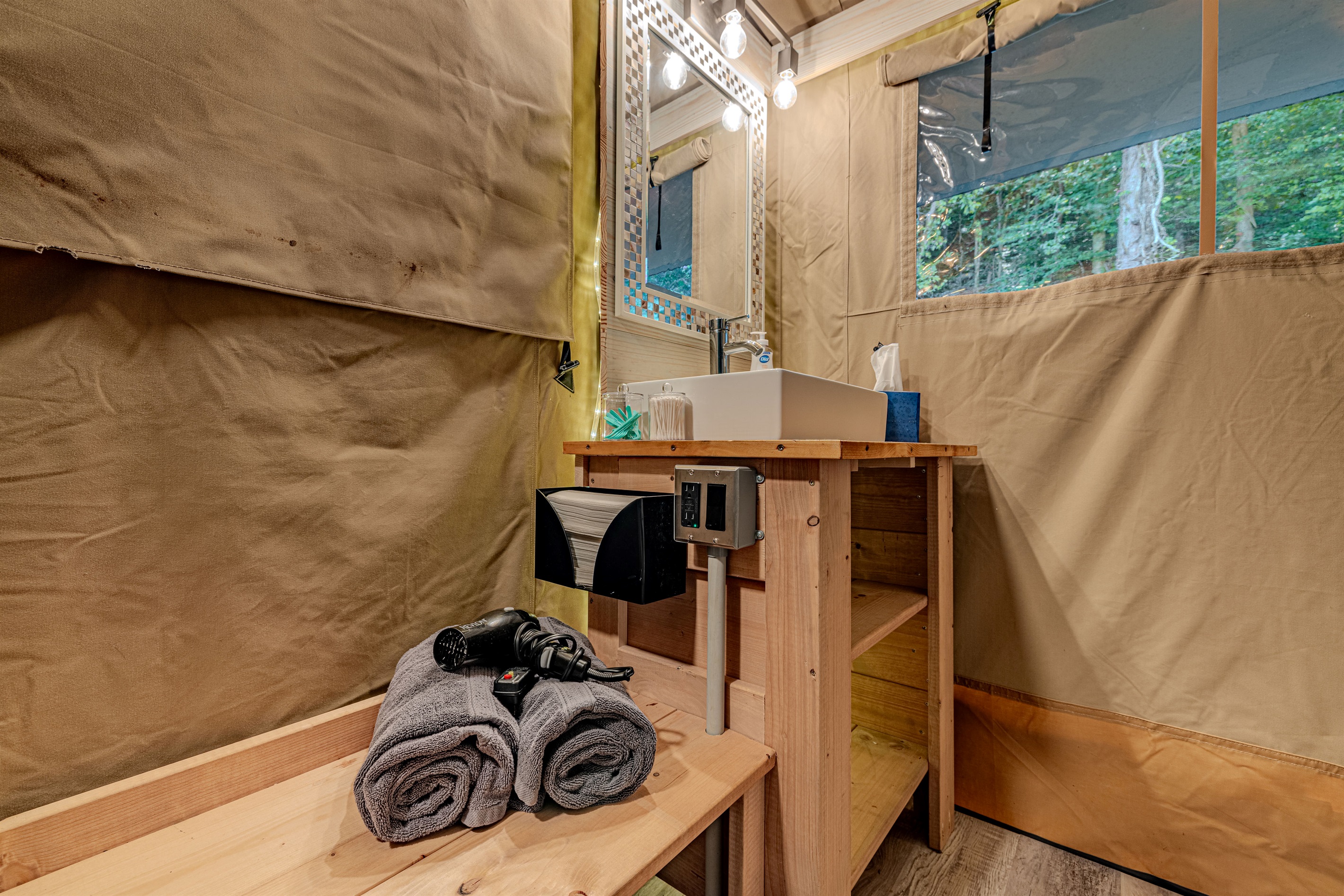 Glamping means no roughing it. Enjoy the convenience of a dedicated vanity area with a stylish vessel sink, lit mirror, and shelves for your personal items.