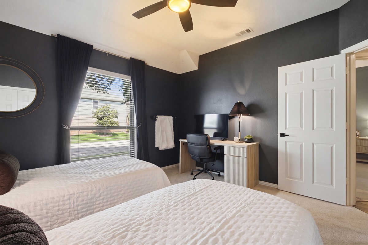 Guest Bedroom 3 with a dedicated workspace including a desk and office chair, plus a 55-inch Smart TV. Bright window keeps the space airy and inviting.
