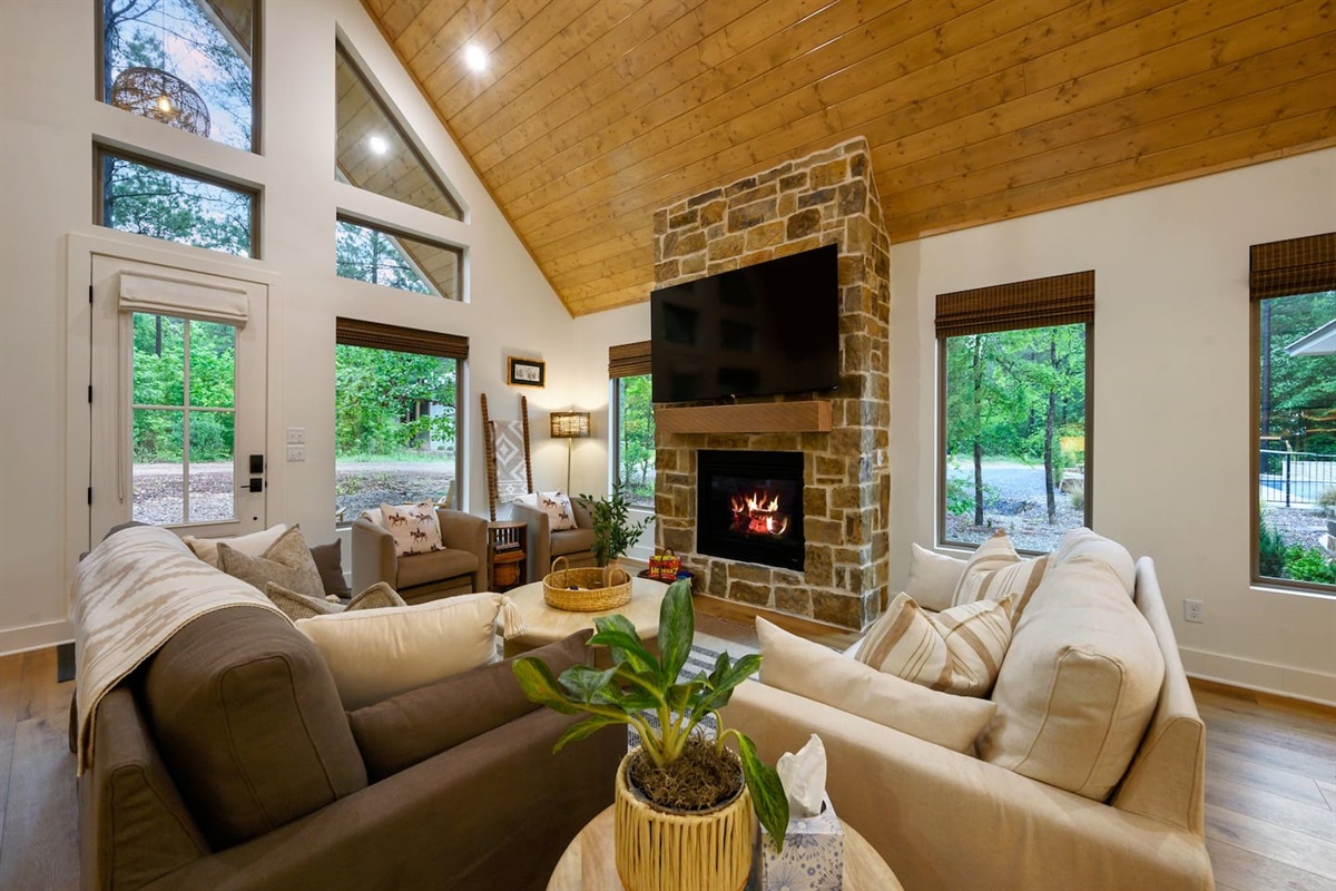 Bathed in natural light with views of the surrounding trees, this living space invites the outdoors in — featuring a striking stone fireplace and thoughtfully curated, organic-inspired furnishings for the perfect balance of comfort and style.