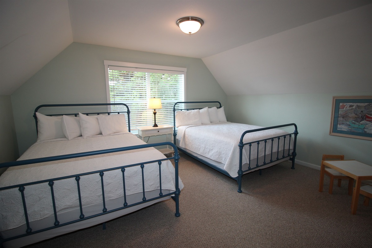 Unwind in the family suite, featuring two queen beds with luxury mattresses and sea-glass-colored walls that perfectly capture the relaxed charm of coastal living.