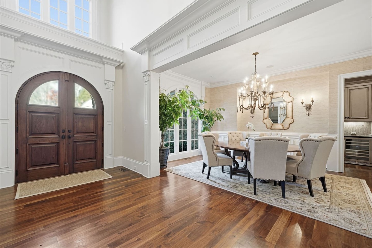 Spacious main dining room to the left of the foyer, featuring a chandelier, seating for seven, and lush green plants. A bright, welcoming space perfect for shared meals or special gatherings.