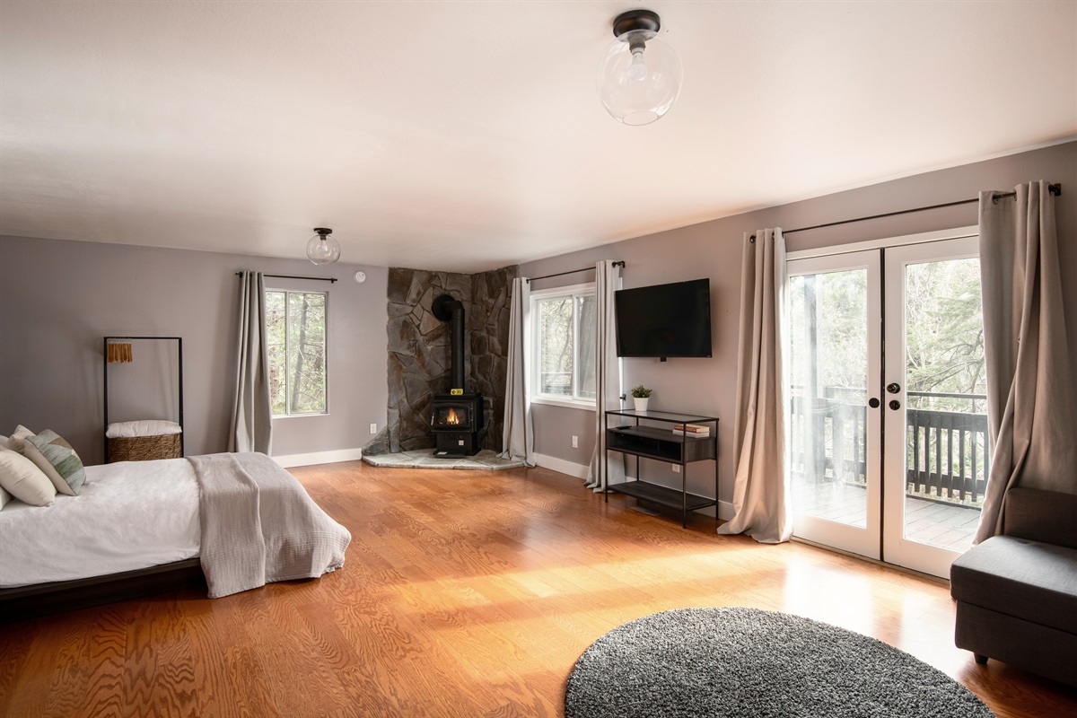 Spacious primary bedroom with cozy fireplace, private deck access, and plenty of natural light—your own peaceful retreat in the trees.