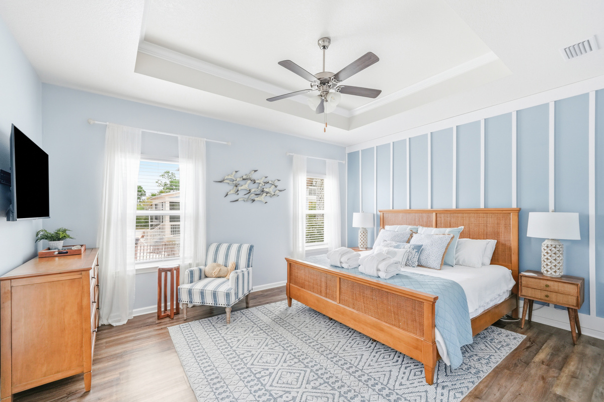 Primary Suite: Elegant King bedroom featuring an en suite bathroom, plush linens, ceiling fan, elegant bedside lamps, dresser, couch, and Smart TV.