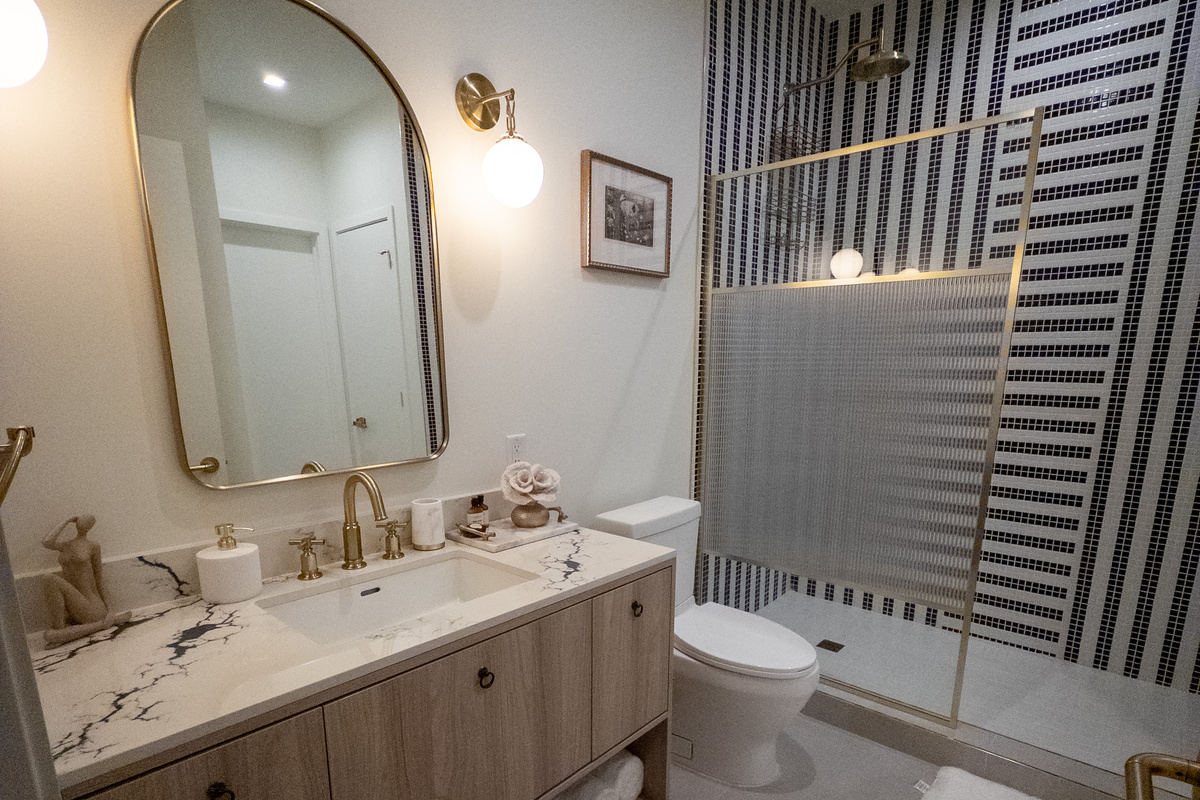 Start the day in a spa-style bath with a walk-in rainfall shower, designer tilework and warm brushed-gold fixtures.