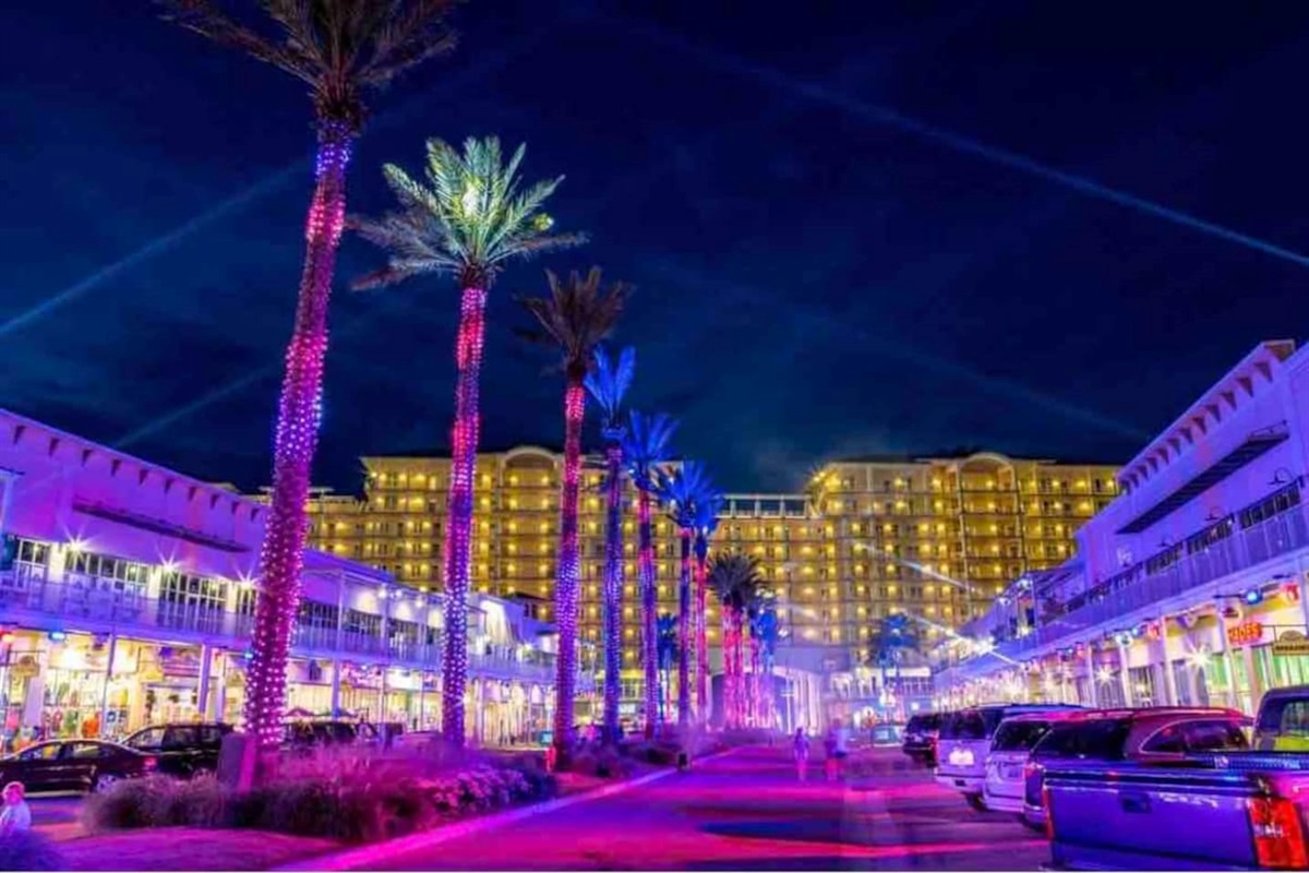 Experience the vibrant nightlife at a tropical resort with illuminated palm trees and bustling shops.
