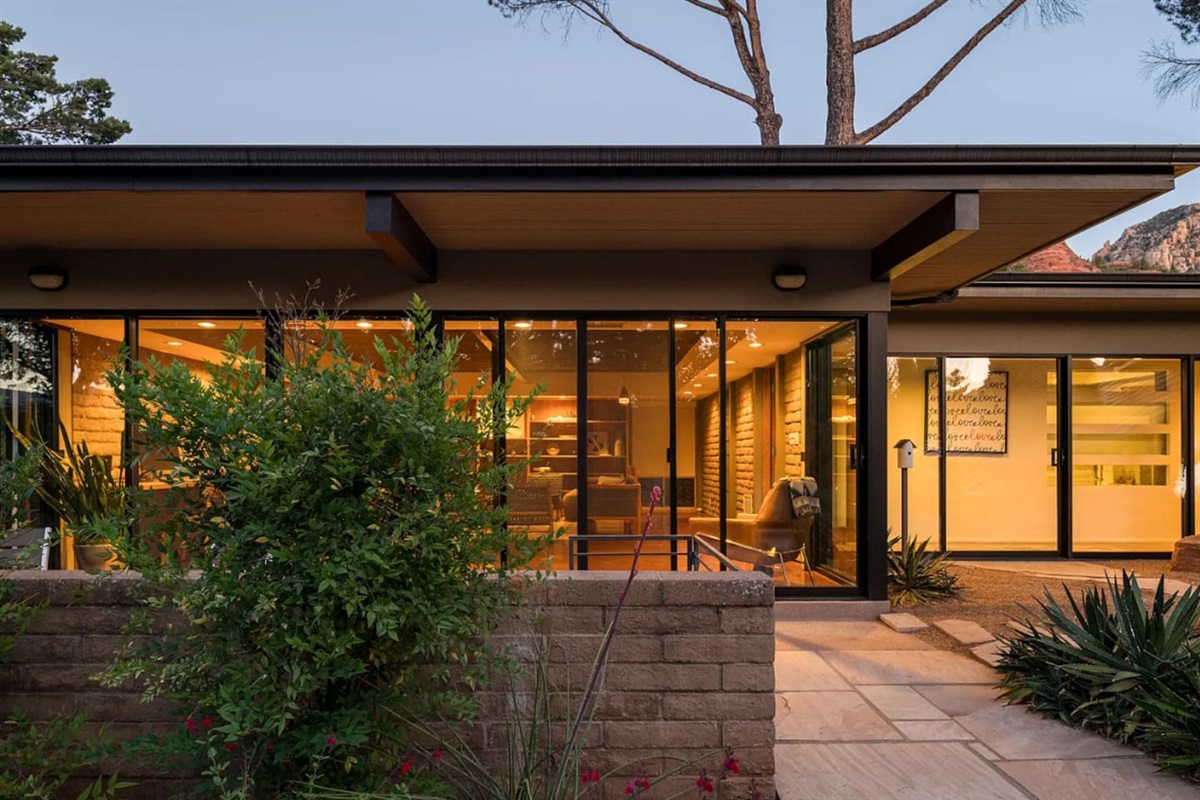 Warmly lit living spaces showcased through expansive glass walls, blending indoor comfort with serene outdoor surroundings at dusk.