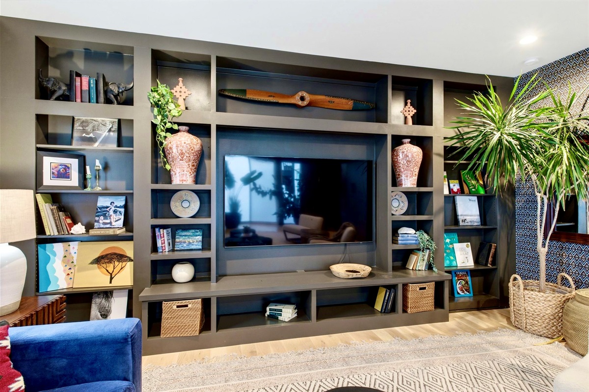 Built-in entertainment wall w/ shelving, TV & lush plants — stylish, functional & full of character.
